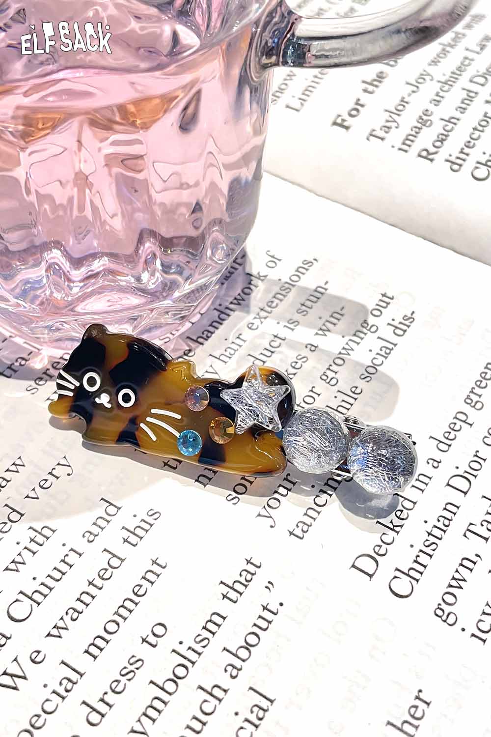 ELFSACK acetate kitten hairpin featuring colorful gems and a playful design on a book page