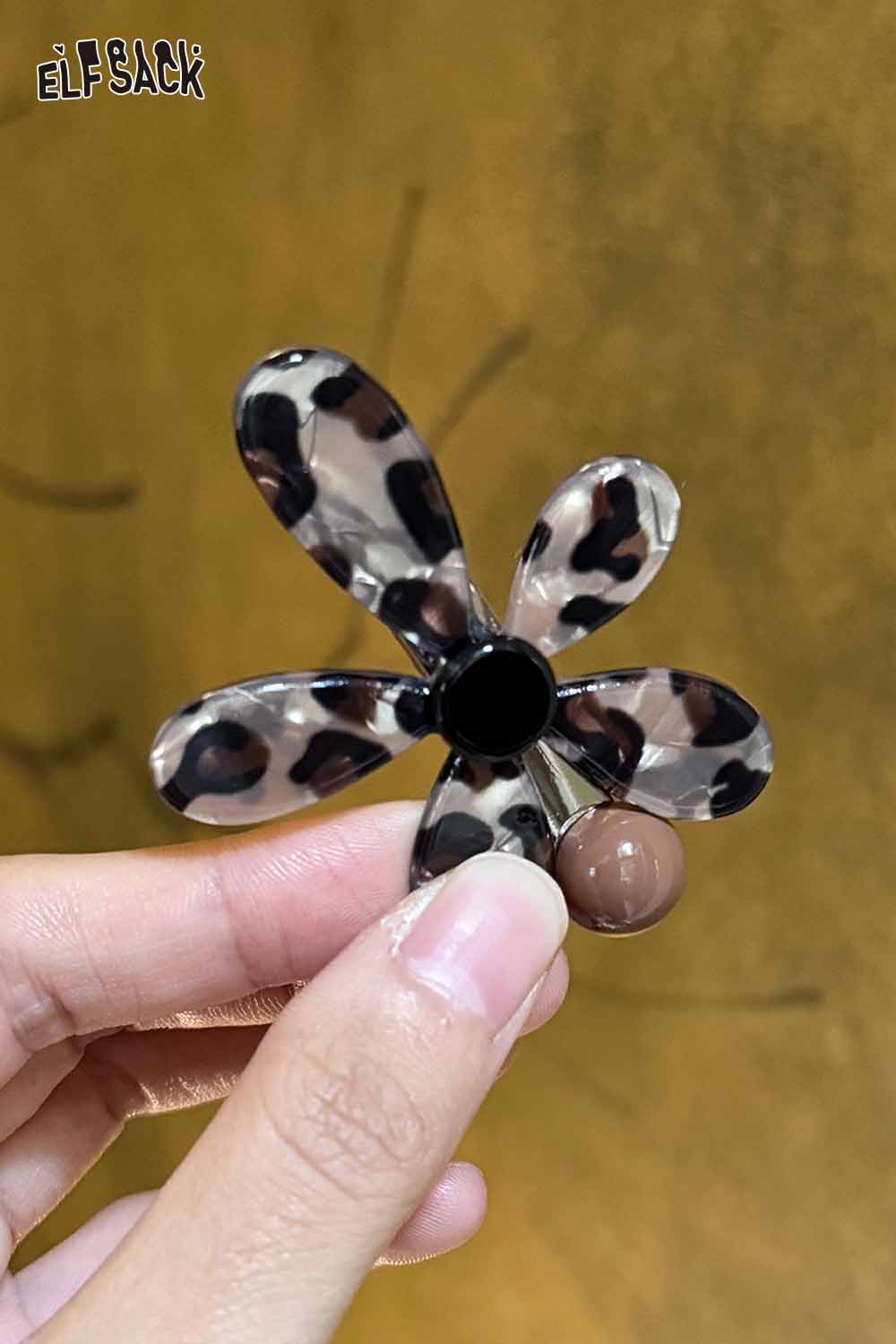 ELFSACK asymmetric floral hairpin in a leopard print design held between fingers
