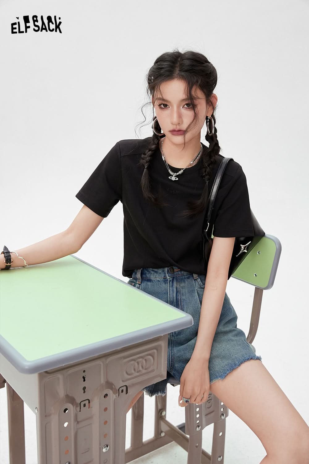 ELFSACK black BM Style T-shirt worn by woman sitting on green and gray school desk chair