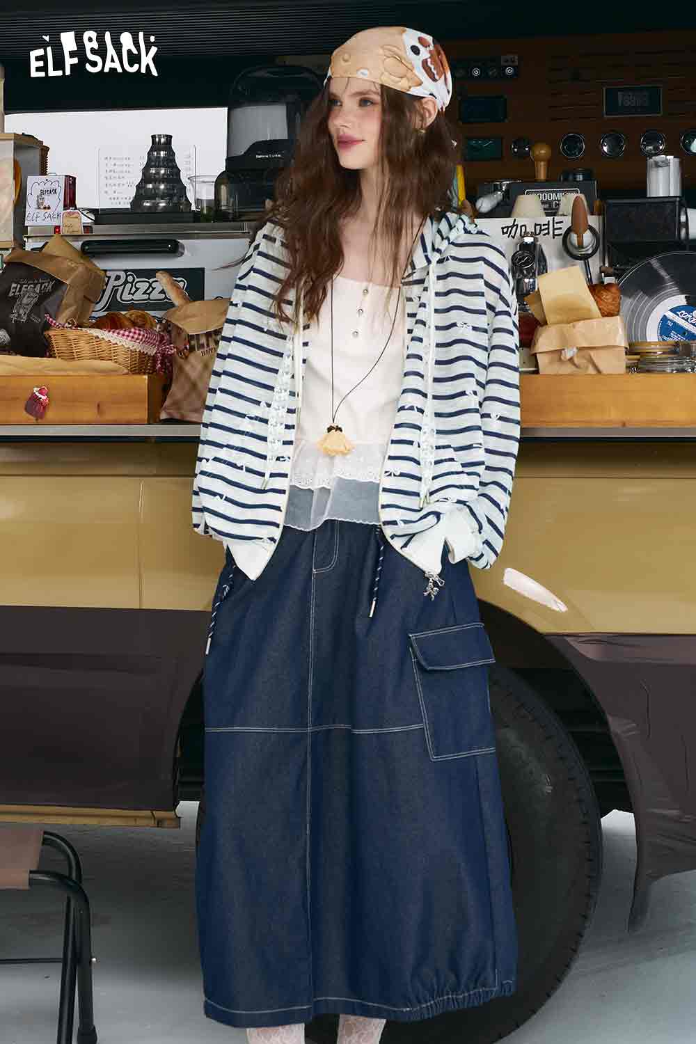 ELFSACK model wearing oversized striped cardigan for women with hood over white tank top and denim wide skirt by food truck