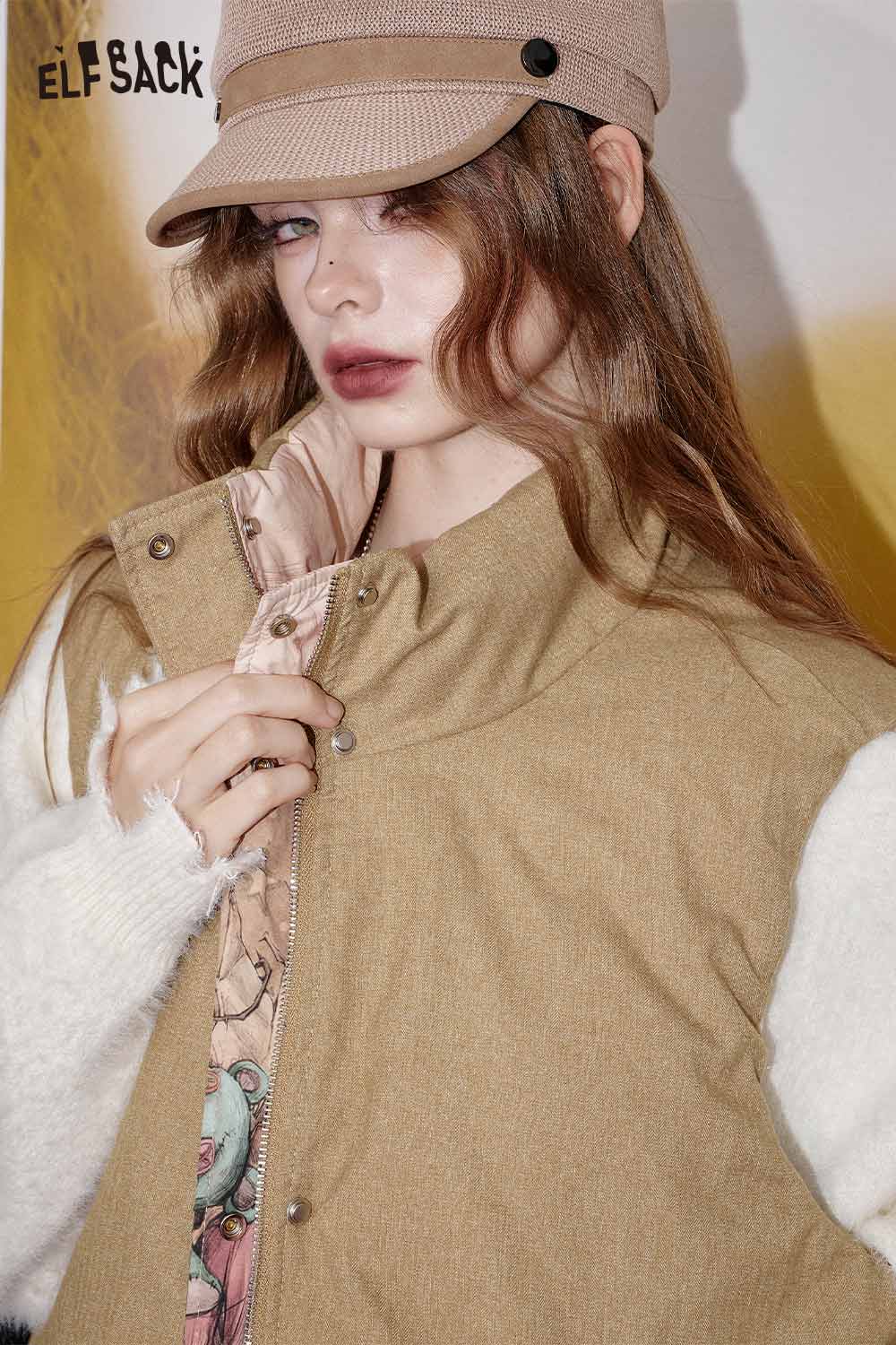 ELFSACK cartoon graphic puffer vest in beige, styled with a trendy cap for a fashion-forward look