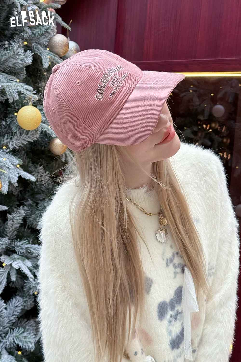 Woman wearing a pink corduroy baseball cap for women with embroidered logo, set against a festive background