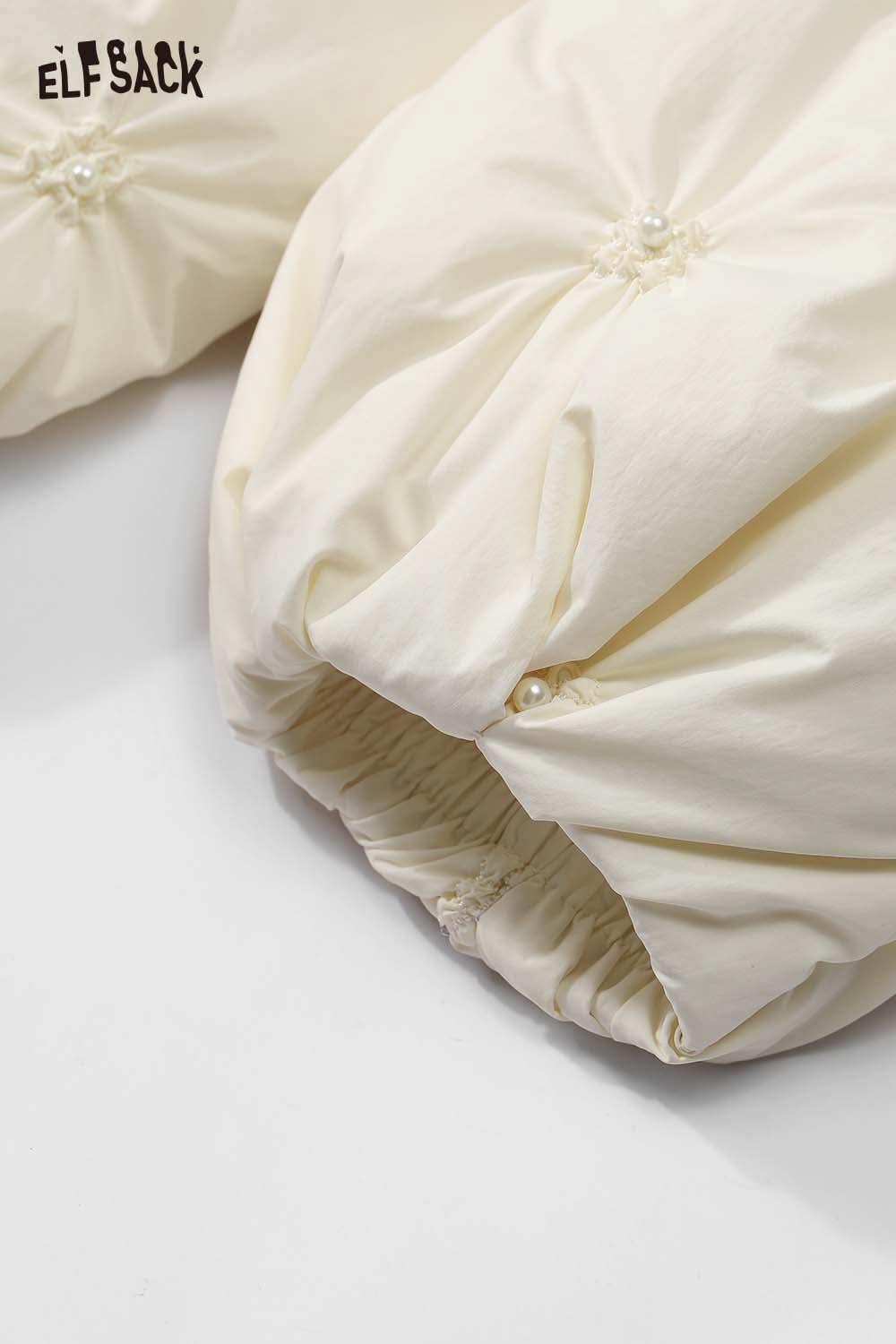 Close-up of ELFSACK cream quilted mid-length jacket showcasing pearl detailing and gathered sleeves