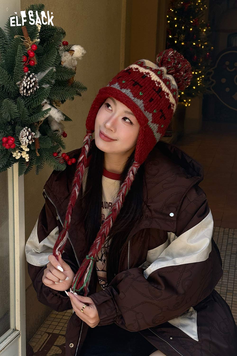 Model wearing a cute Fair Isle knit beanie with a pom-pom and braided ties, styled for winter fashion.