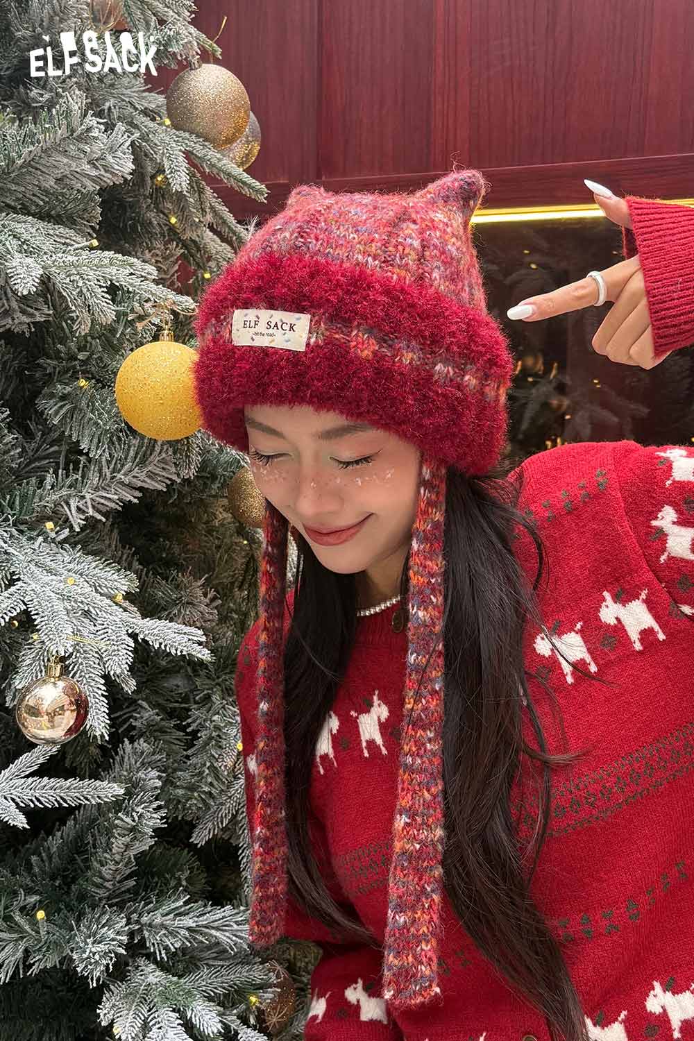 Woman wearing a cute cat ear beanie for women with colorful patterns, posing beside a decorated Christmas tree