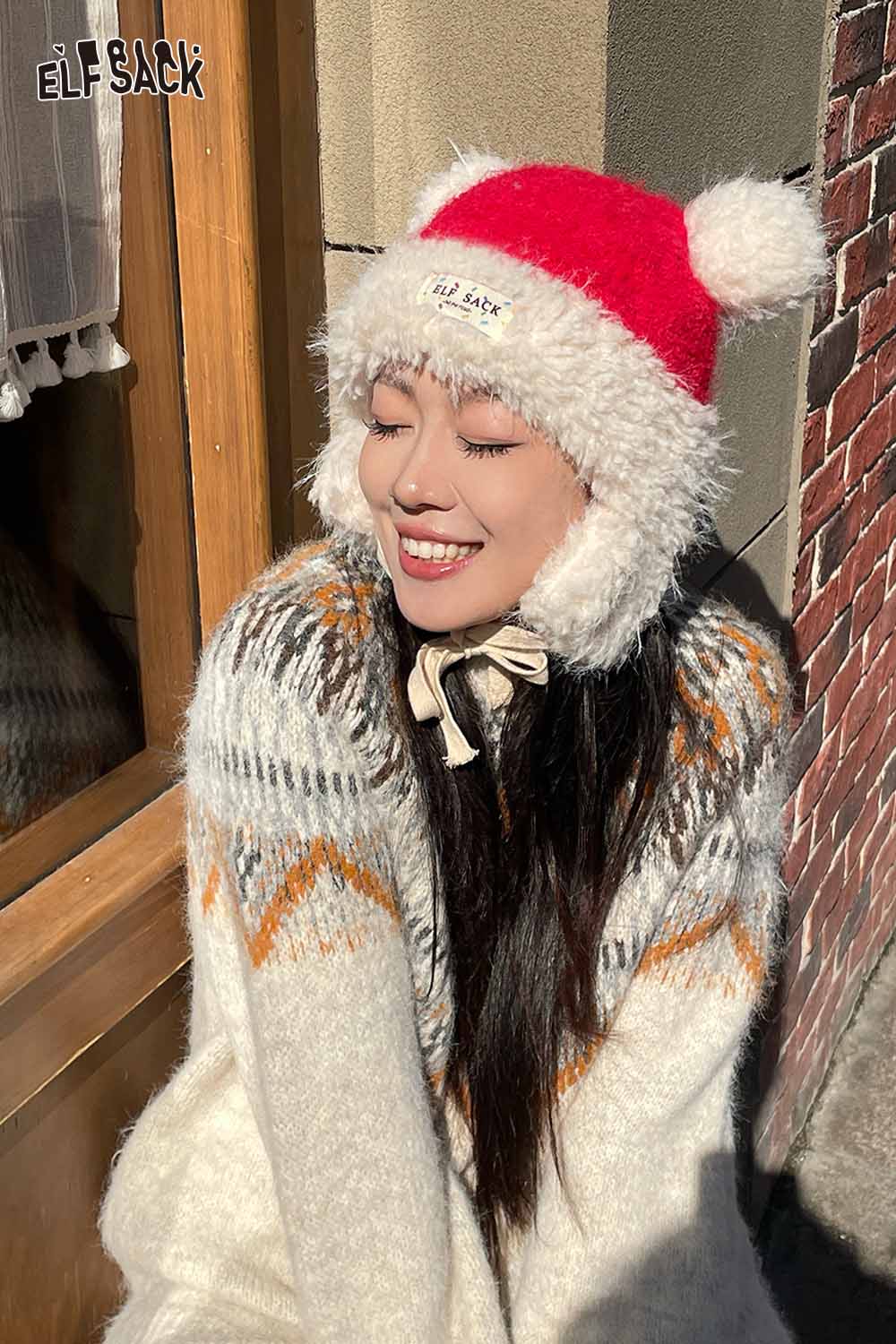Smiling model wearing a cute plush ear flap hat with a red and white design and cozy winter sweater