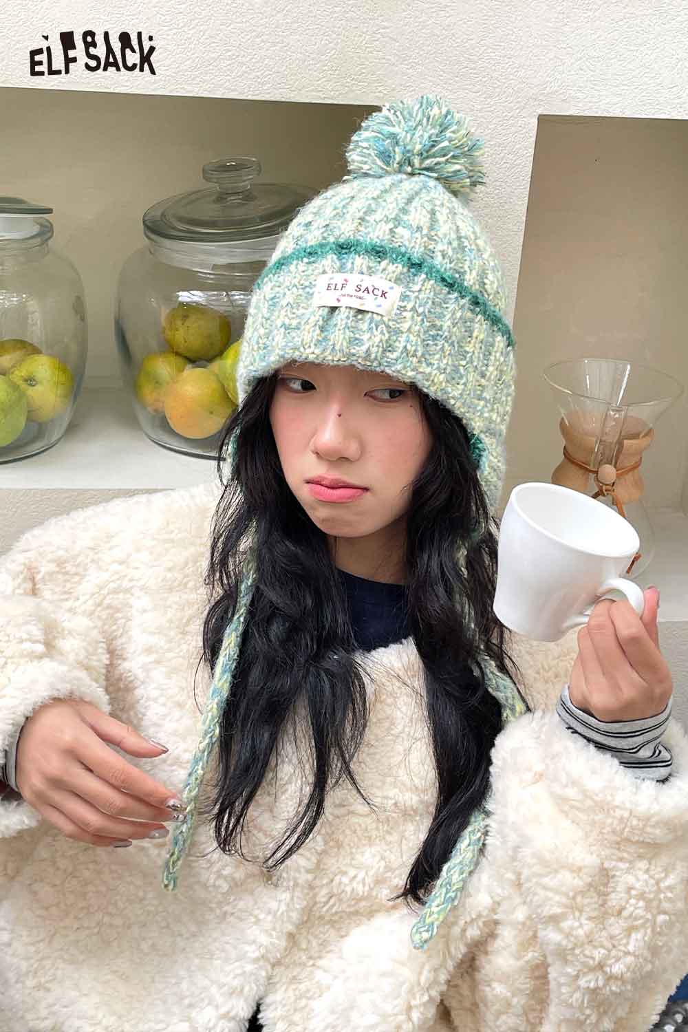 Cute striped pom beanie for women in light colors worn by a model holding a white mug