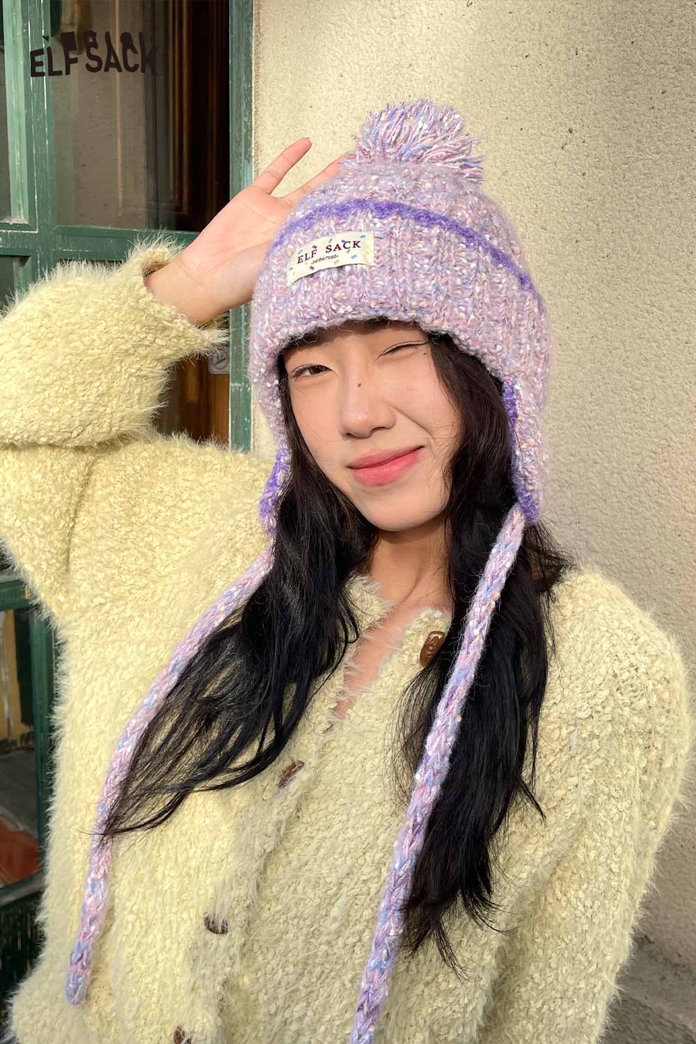 Woman wearing a cute striped pom beanie for women with playful purple tones and braided ties