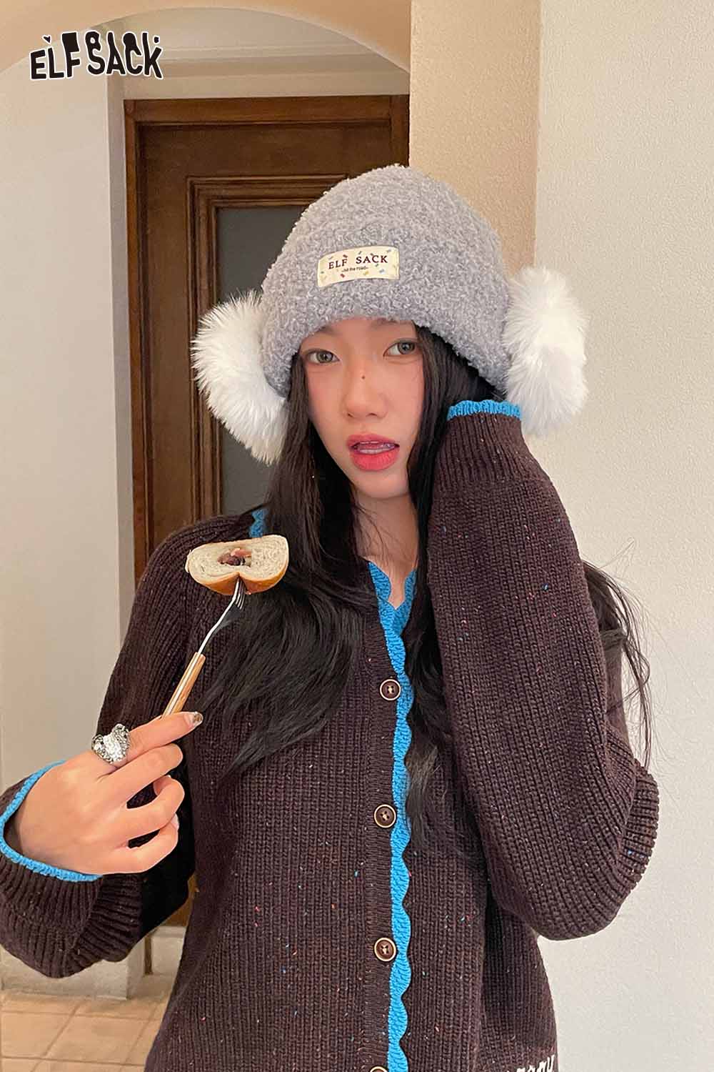 ELFSACK model wearing a cozy gray white plush ear muff beanie with fluffy accents for winter style