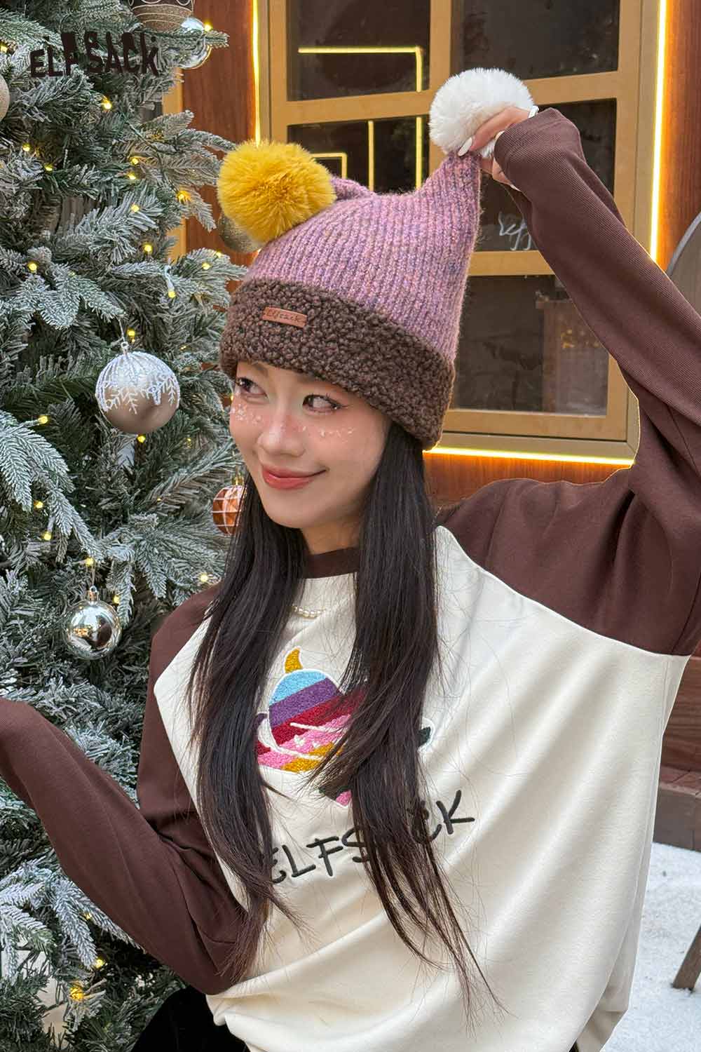 Stylish woman wearing a colorful pom pom knit beanie with festive holiday decor in the background
