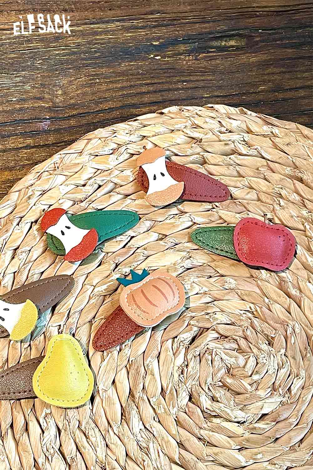 Colorful genuine leather fruit hairpins arranged on a woven mat, featuring various fruit designs.