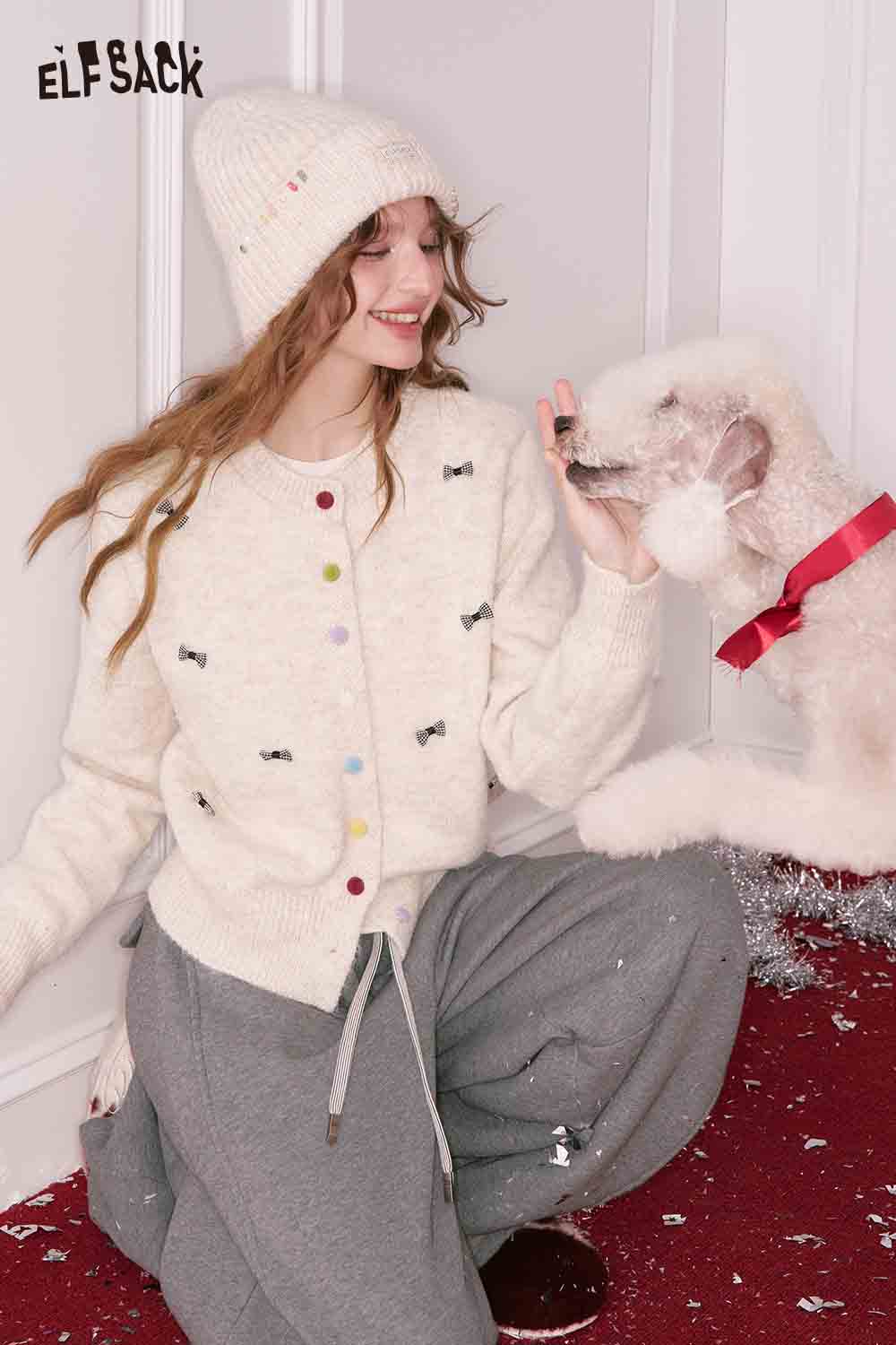 ELFSACK girly bow cardigan in cream with colorful buttons, styled with a cozy hat and playful dog