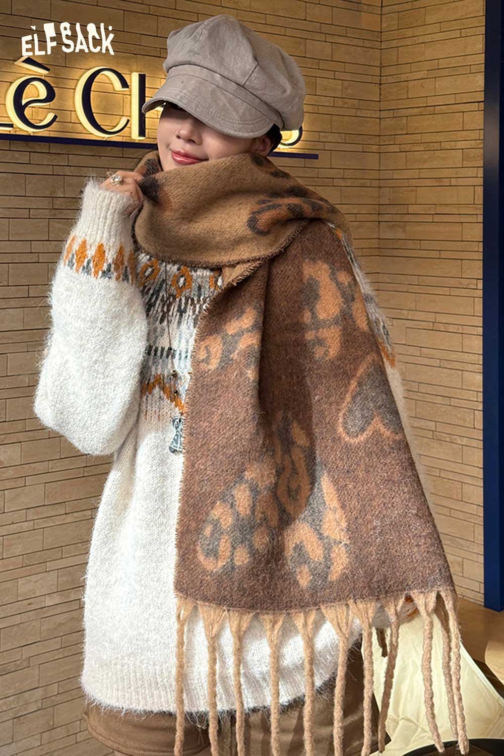ELFSACK leopard heart fringe scarf in warm tones draped stylishly over a model wearing a cozy sweater