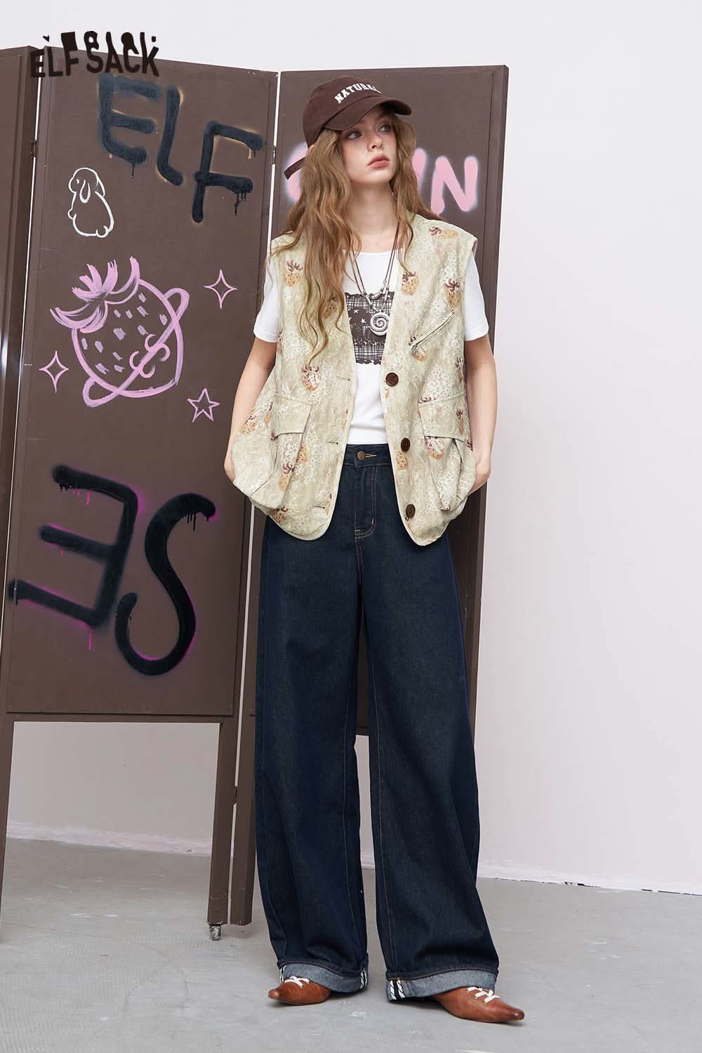 ELFSACK women's graphic lace vest layered over graphic tee with embroidered details paired with wide leg jeans and cap