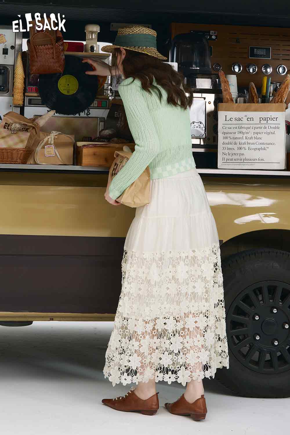 Model wearing mint checkered knit cardigan with white lace maxi skirt straw hat and brown flats at food truck