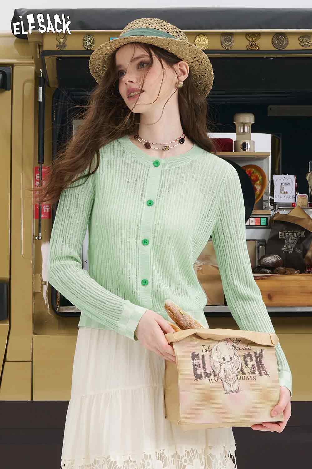 ELFSACK model wearing mint checkered knit cardigan with green buttons over white skirt holding branded tote and straw hat