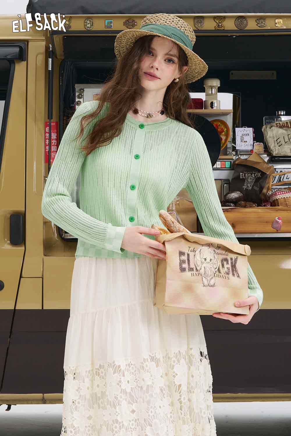 Model wearing ELFSACK mint checkered knit cardigan with green buttons straw hat and lace maxi skirt holding canvas bag
