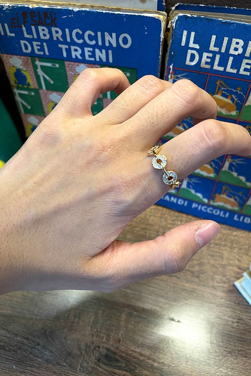 ELFSACK minimalist copper coin ring displayed on a hand with vintage books in the background