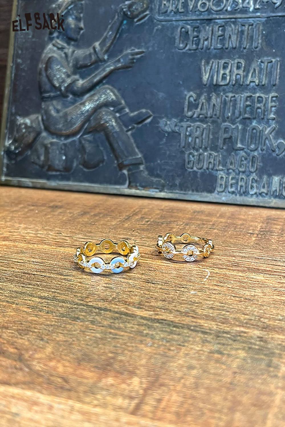 Two minimalist copper coin rings by ELFSACK displayed on a wooden surface with artistic backdrop