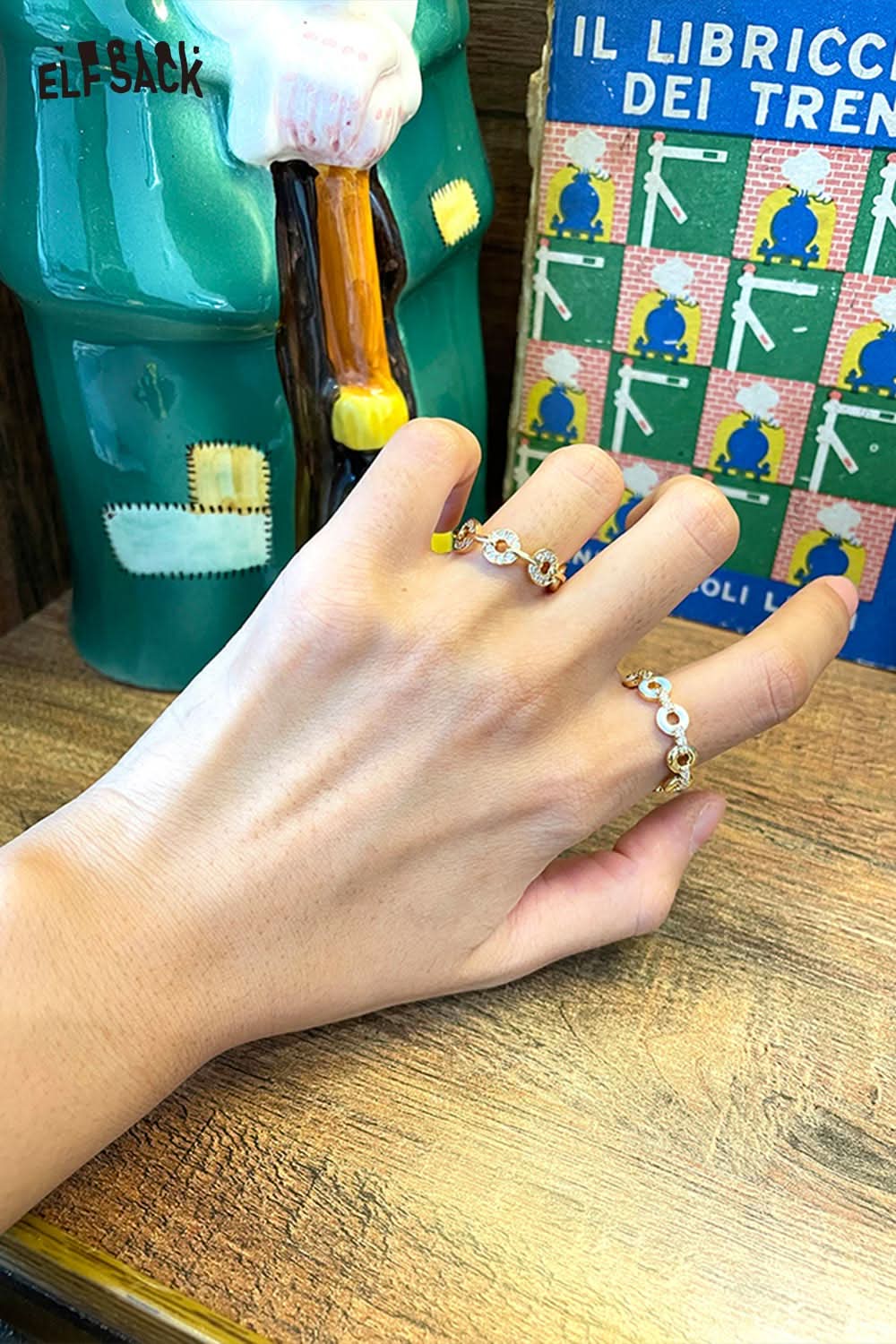 Hand wearing a minimalist copper coin ring alongside a decorative background with colorful books