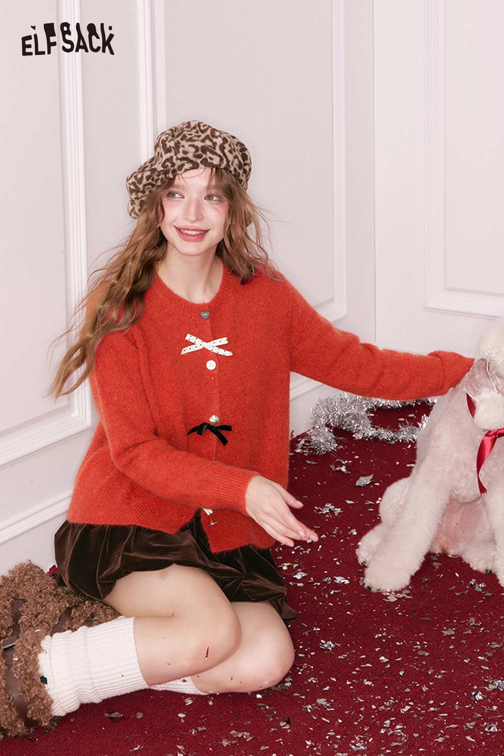 ELFSACK preppy 3D bow cardigan in orange with a playful design, styled with a chic hat and festive backdrop