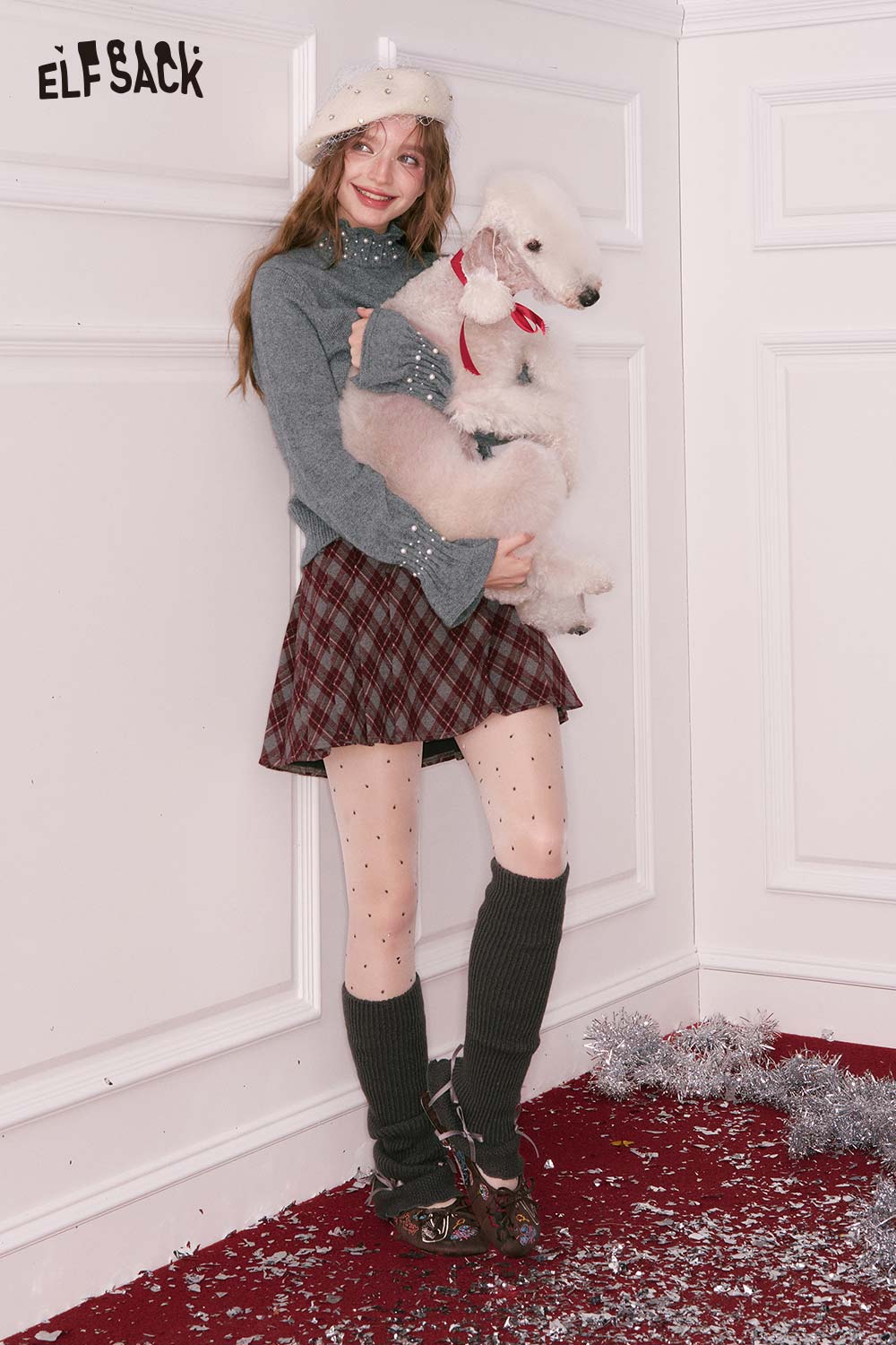 Woman wearing a preppy high neck pearl sweater with a plaid skirt and holding a fluffy dog