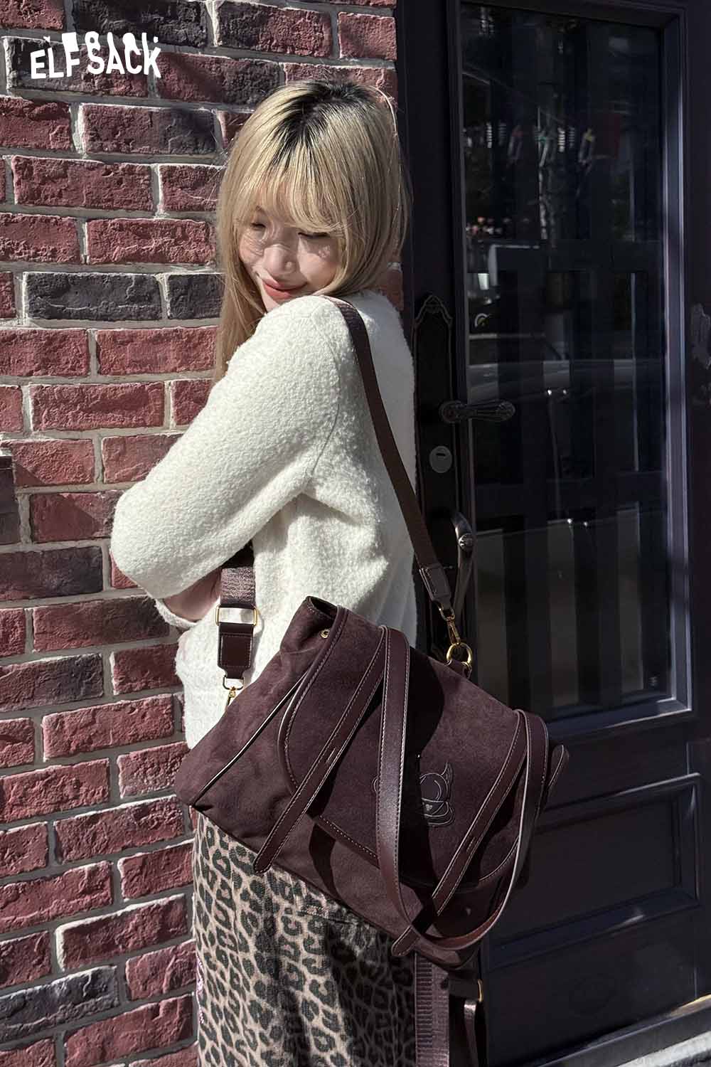 ELFSACK preppy suede backpack for women in burgundy, styled with a cozy outfit against a brick wall