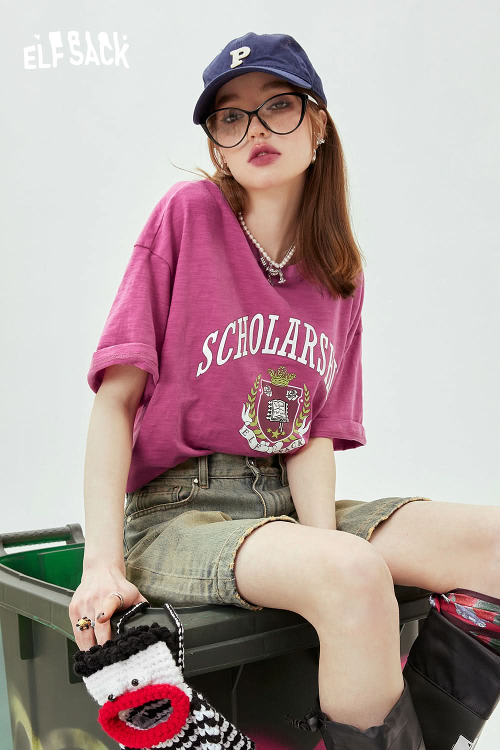 ELFSACK casual oversized purple T-shirt with graphic print worn by woman with glasses and cap