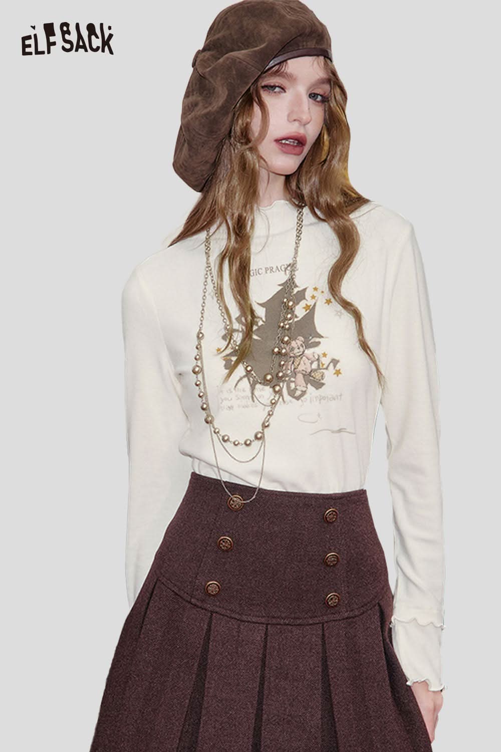ELFSACK cartoon graphic long sleeve top in cream with unique design, styled with a skirt and accessories