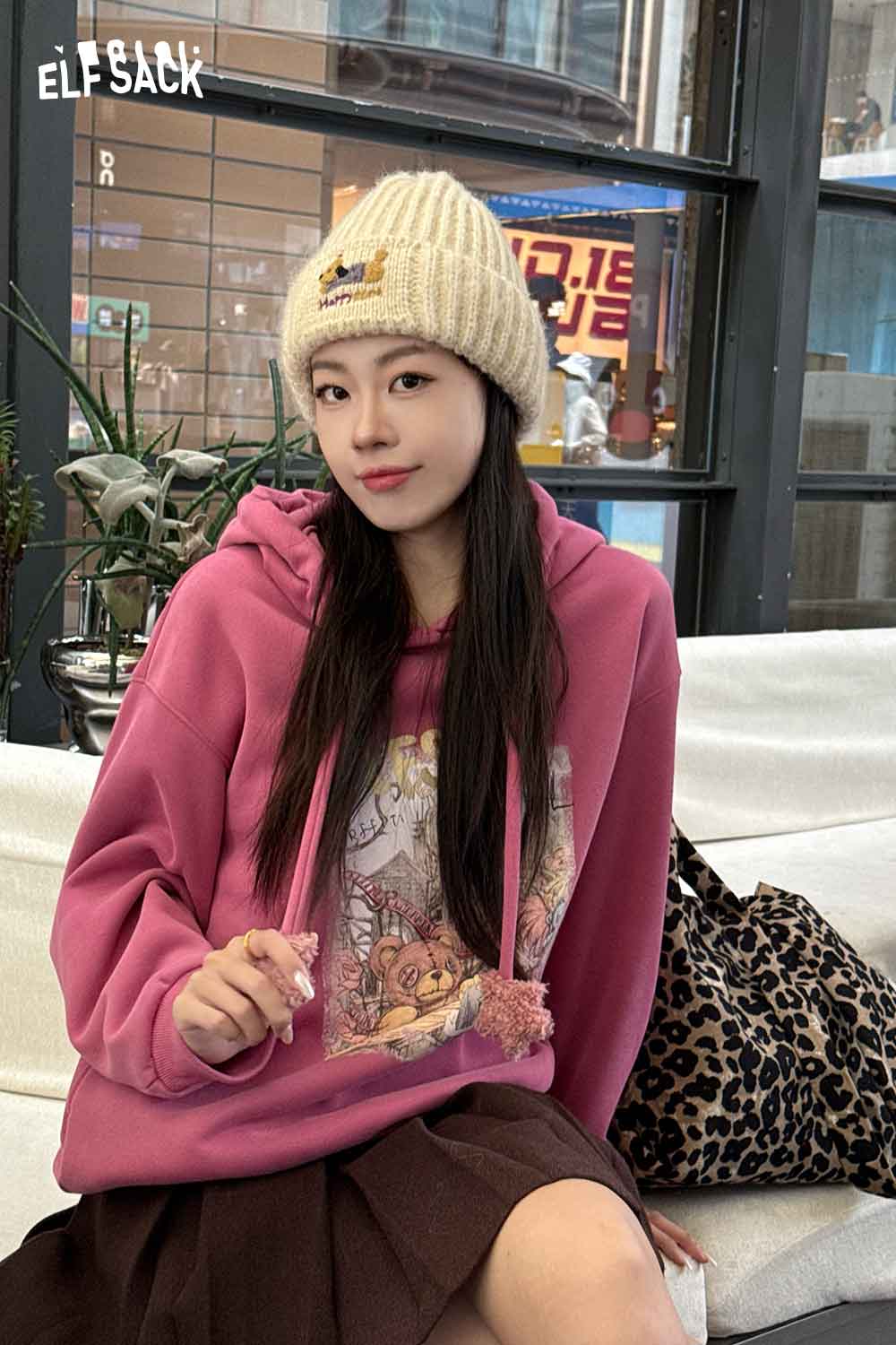 Young woman wearing a cozy hoodie and soft dog embroidered hat, seated in a stylish setting