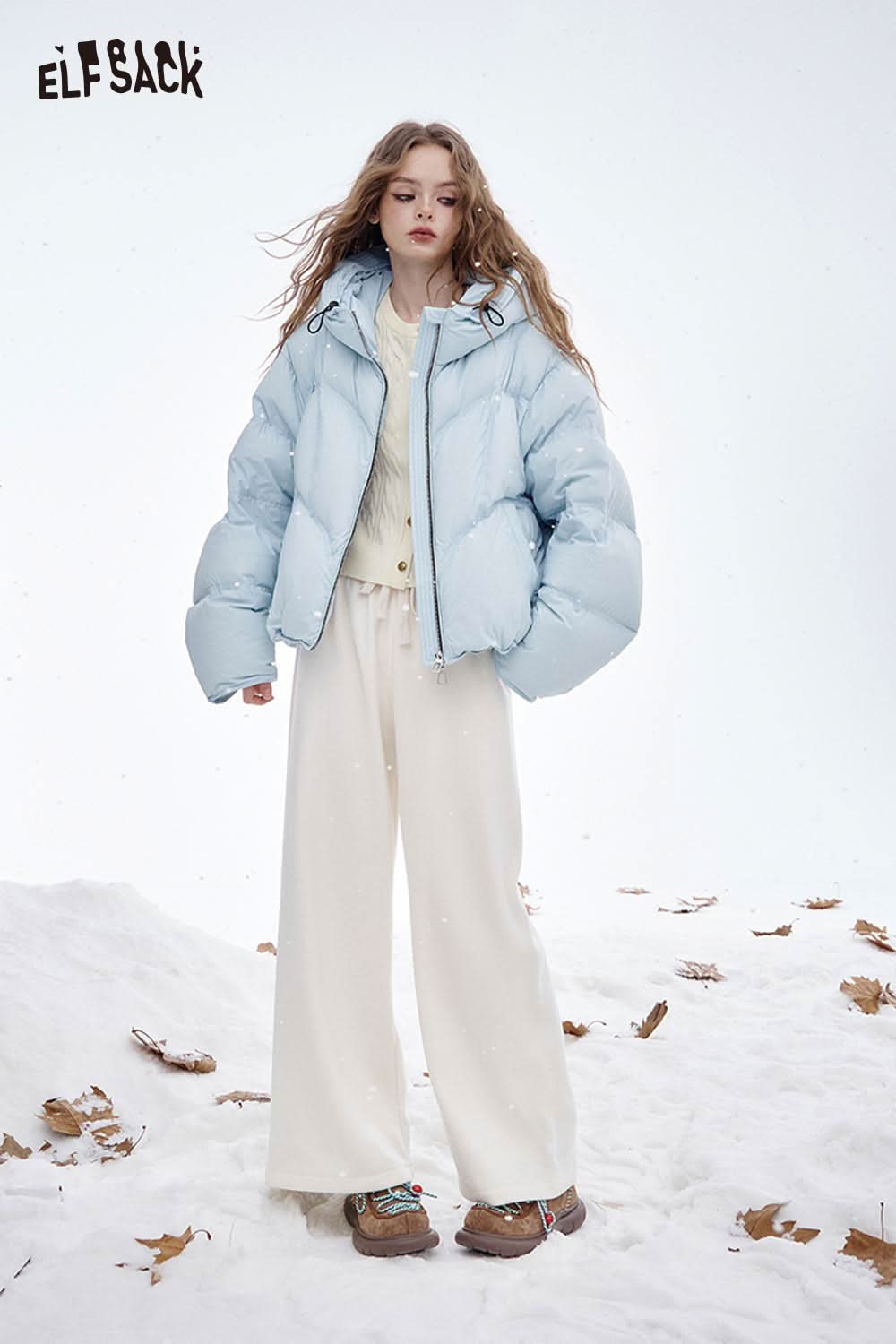 ELFSACK model wearing a soft embroidered knit sweater with a light blue puffer jacket in a snowy setting
