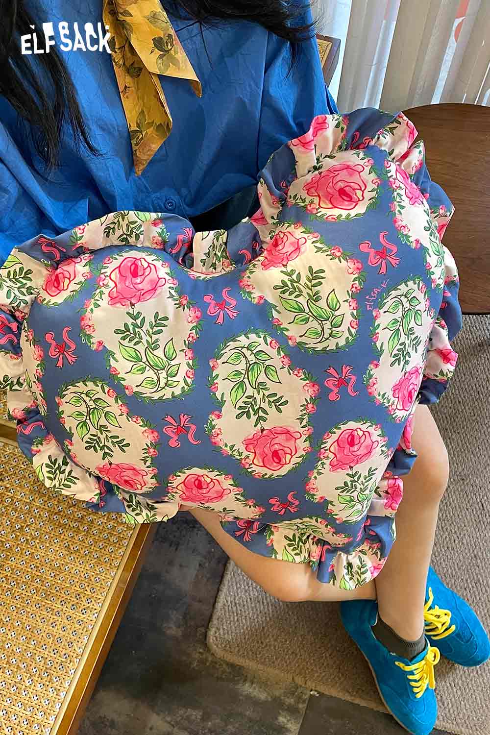 ELFSACK heart shaped rose pillow with pink rose print and ruffle trim held by person in blue outfit