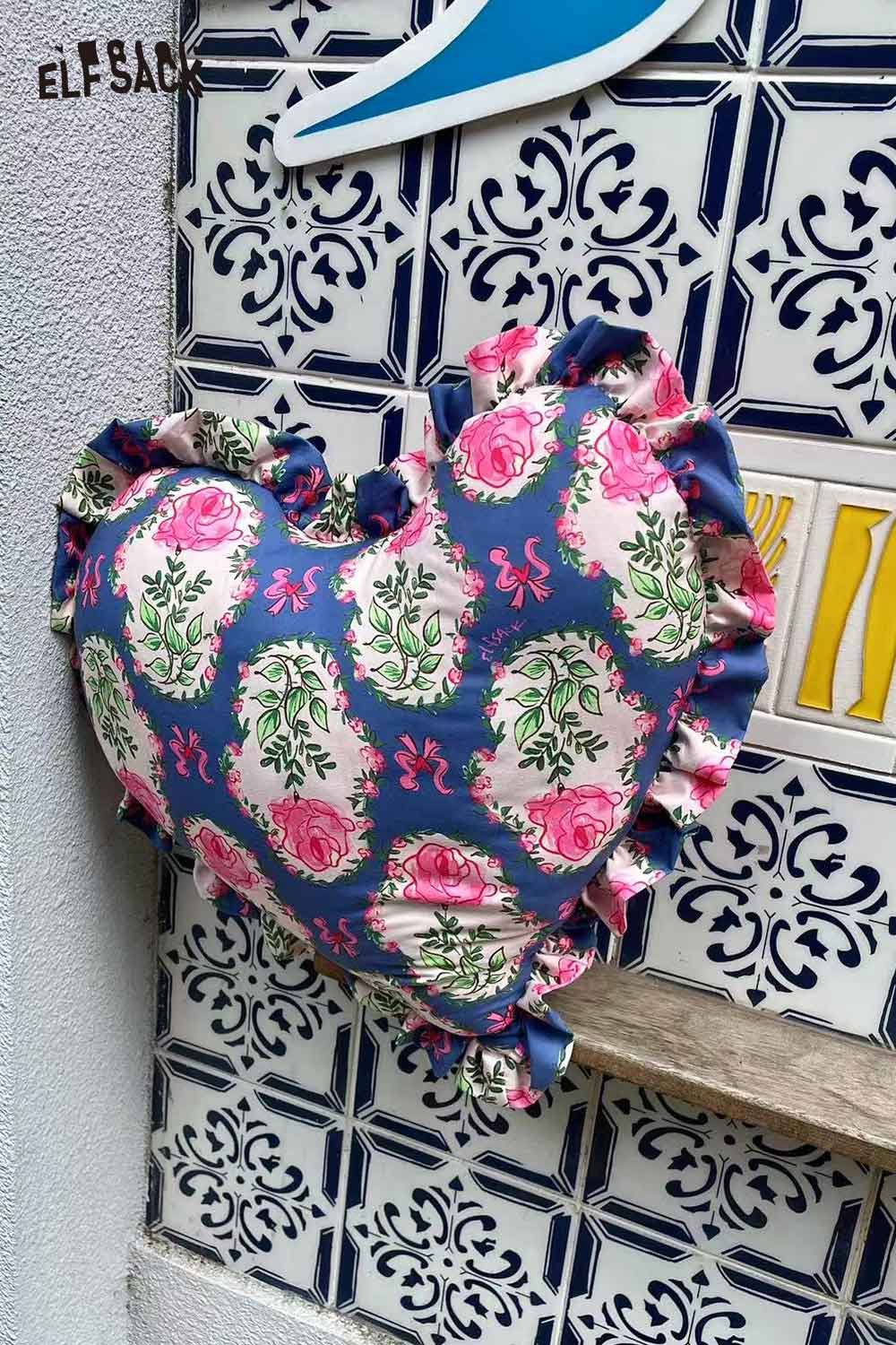 ELFSACK heart shaped rose pillow blue floral print with ruffled edges displayed on decorative tile wall