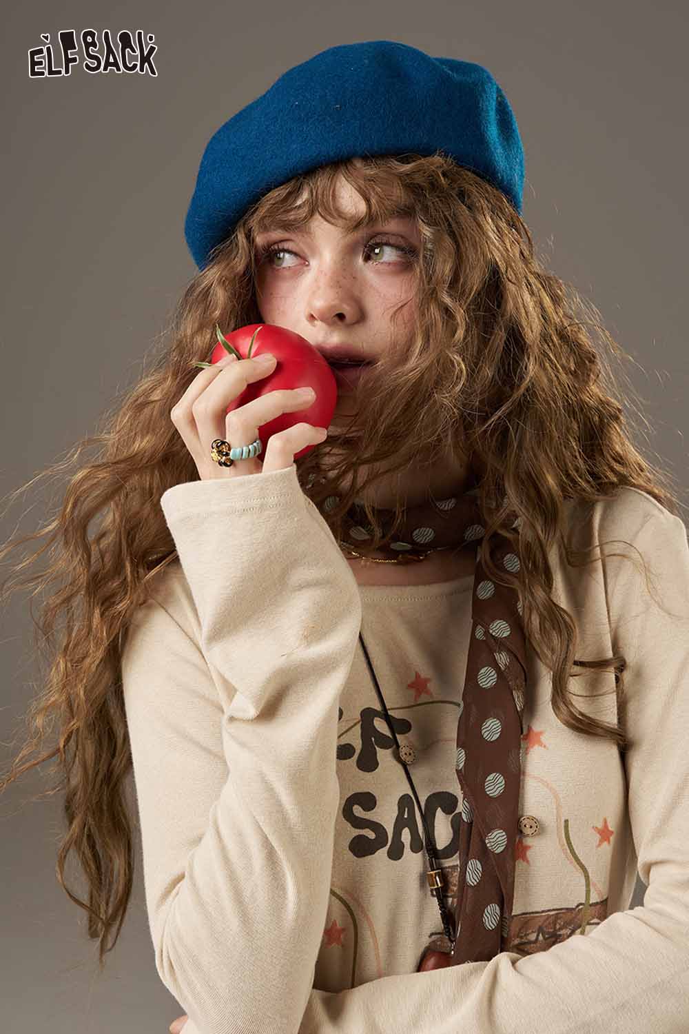 Stylish model holding an apple wearing a soft pumpkin beanie for women with a beige long-sleeve shirt