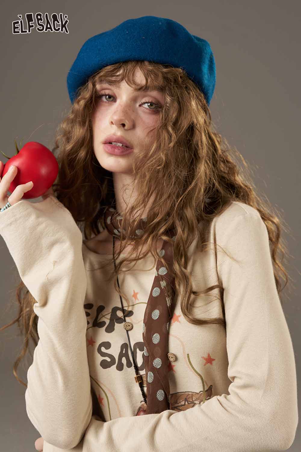 Woman wearing a blue beret holding a tomato, showcasing a soft pumpkin beanie for women