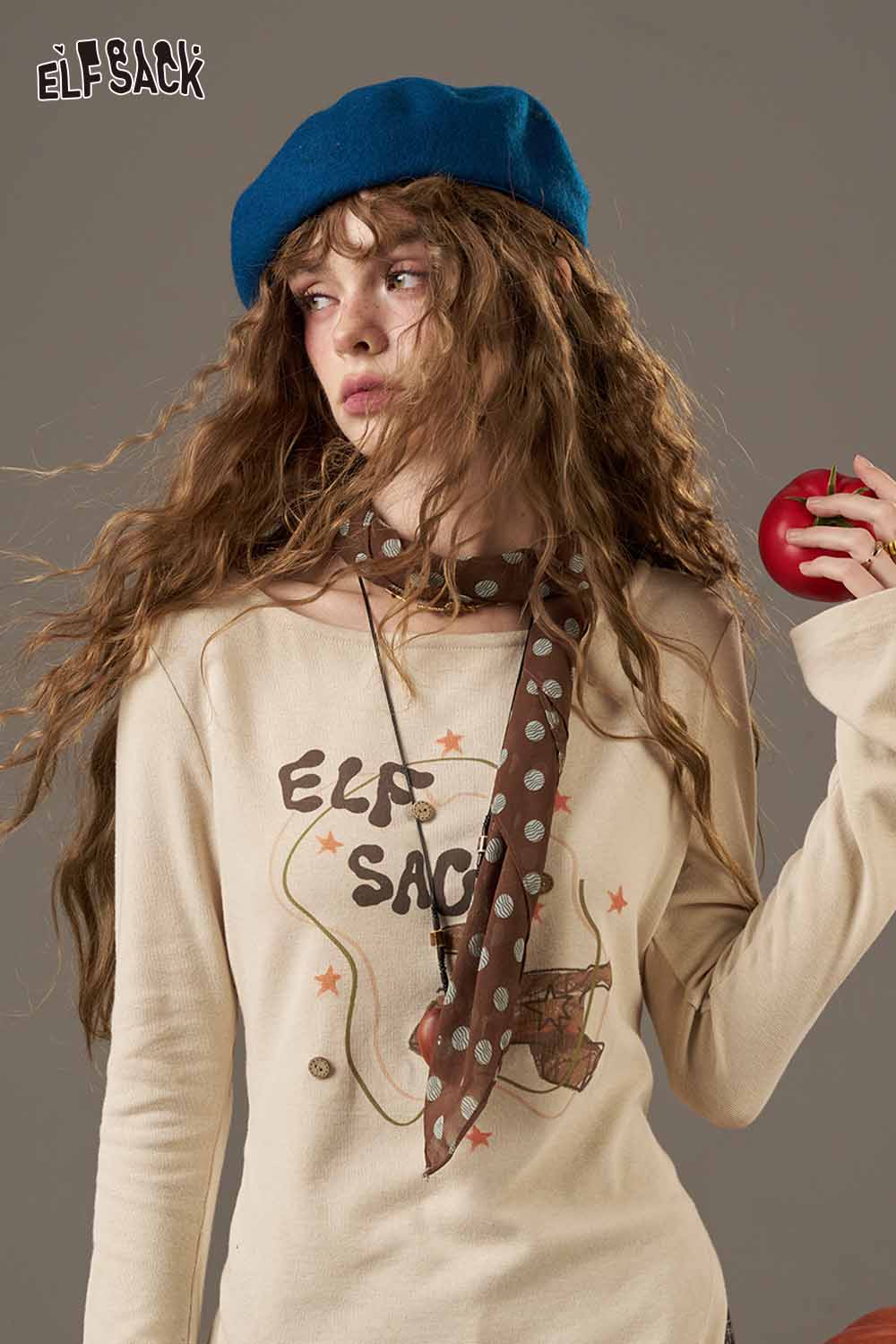 Stylish model wearing a beige top and soft pumpkin beanie for women with a playful apple in hand