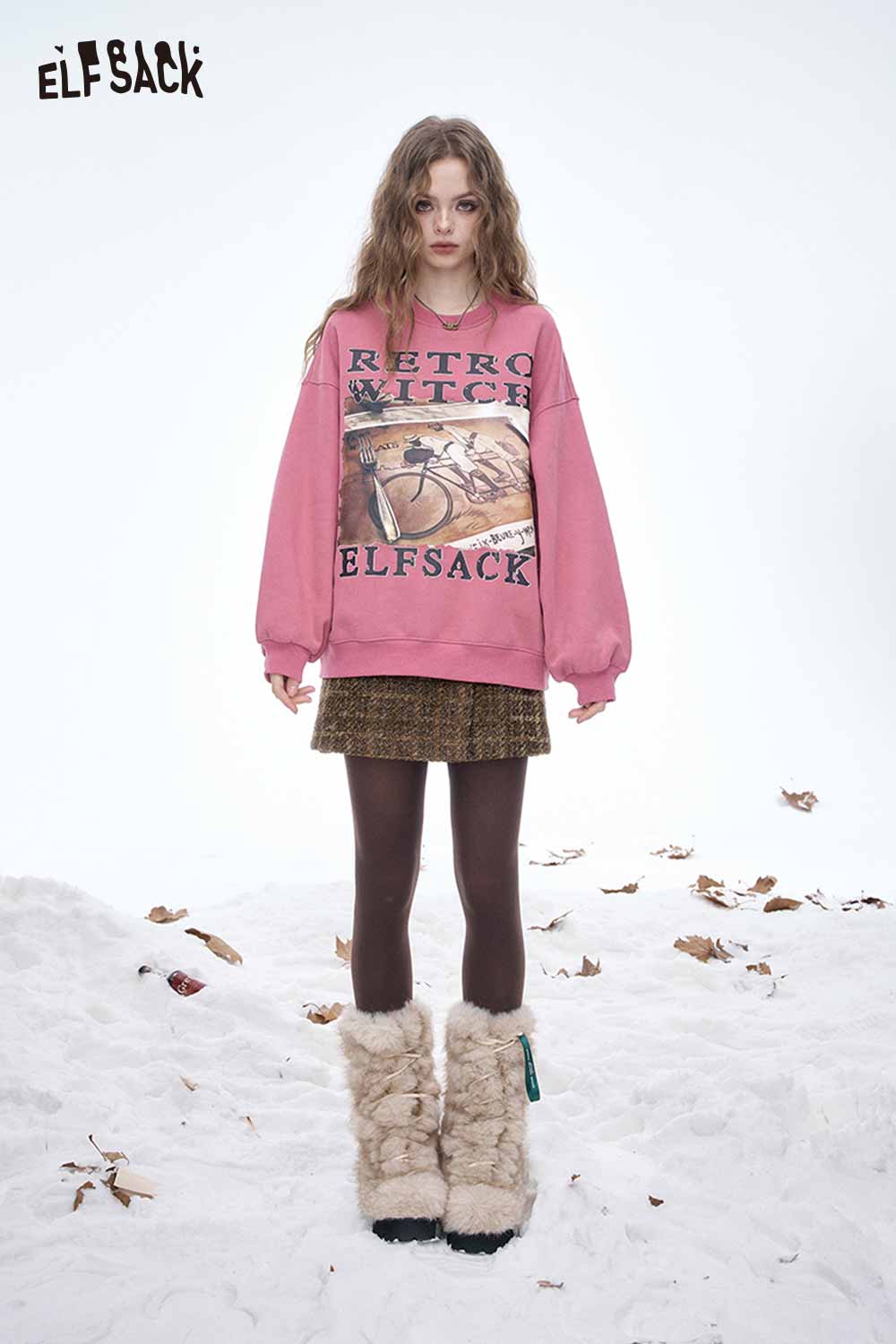 Model wearing a pink sweatshirt and a striped gold button A-line skirt in a snowy outdoor setting