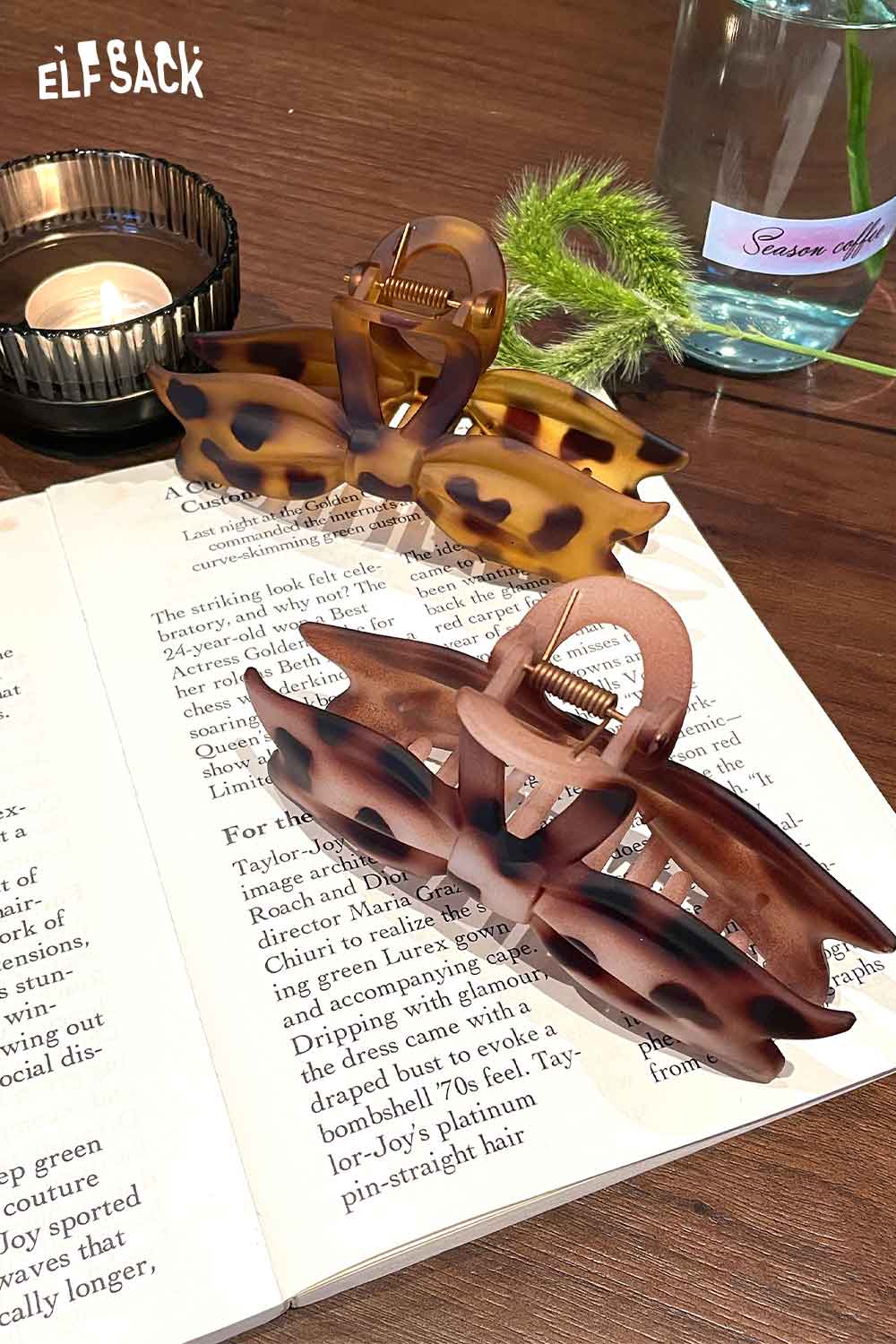 ELFSACK tortoiseshell bow hair claw in two colors placed on a book with a candle and plant
