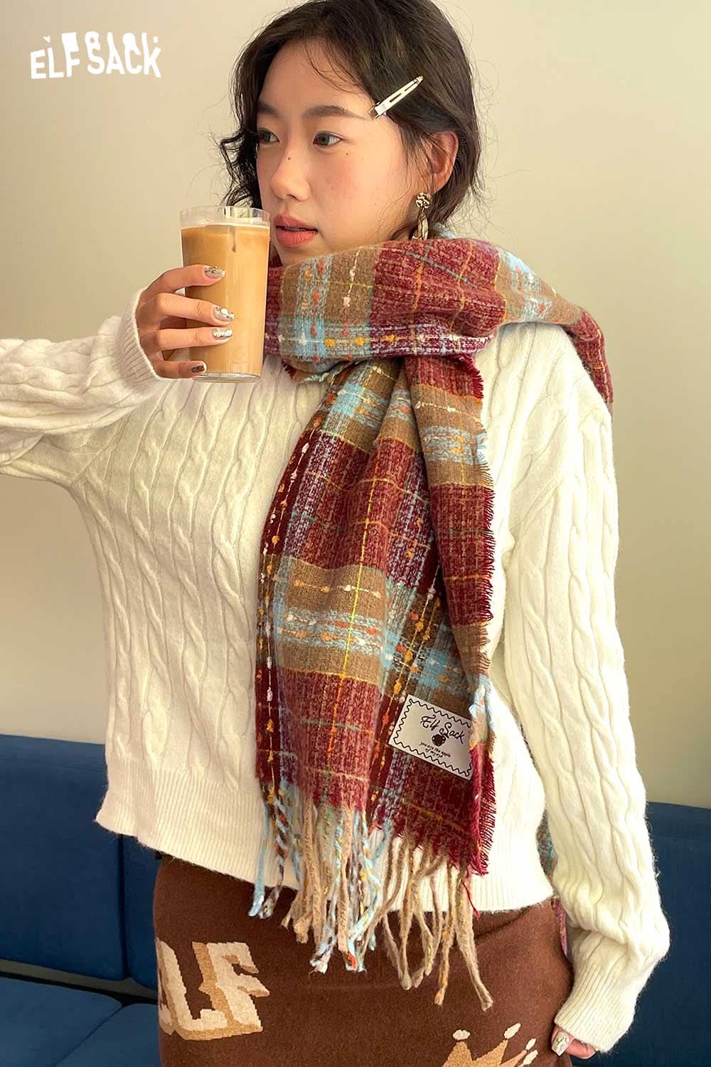 Stylish woman wearing a vintage plaid wool scarf with a cozy white sweater and holding a drink