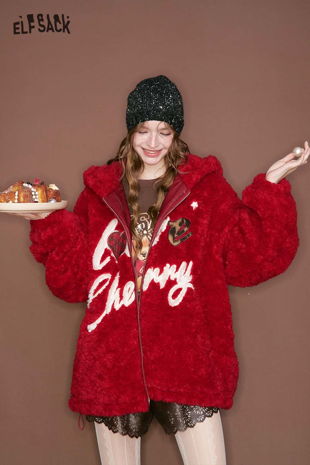 Woman wearing a red ELFSACK fluffy jacket with women's PU leather shorts and a black beanie