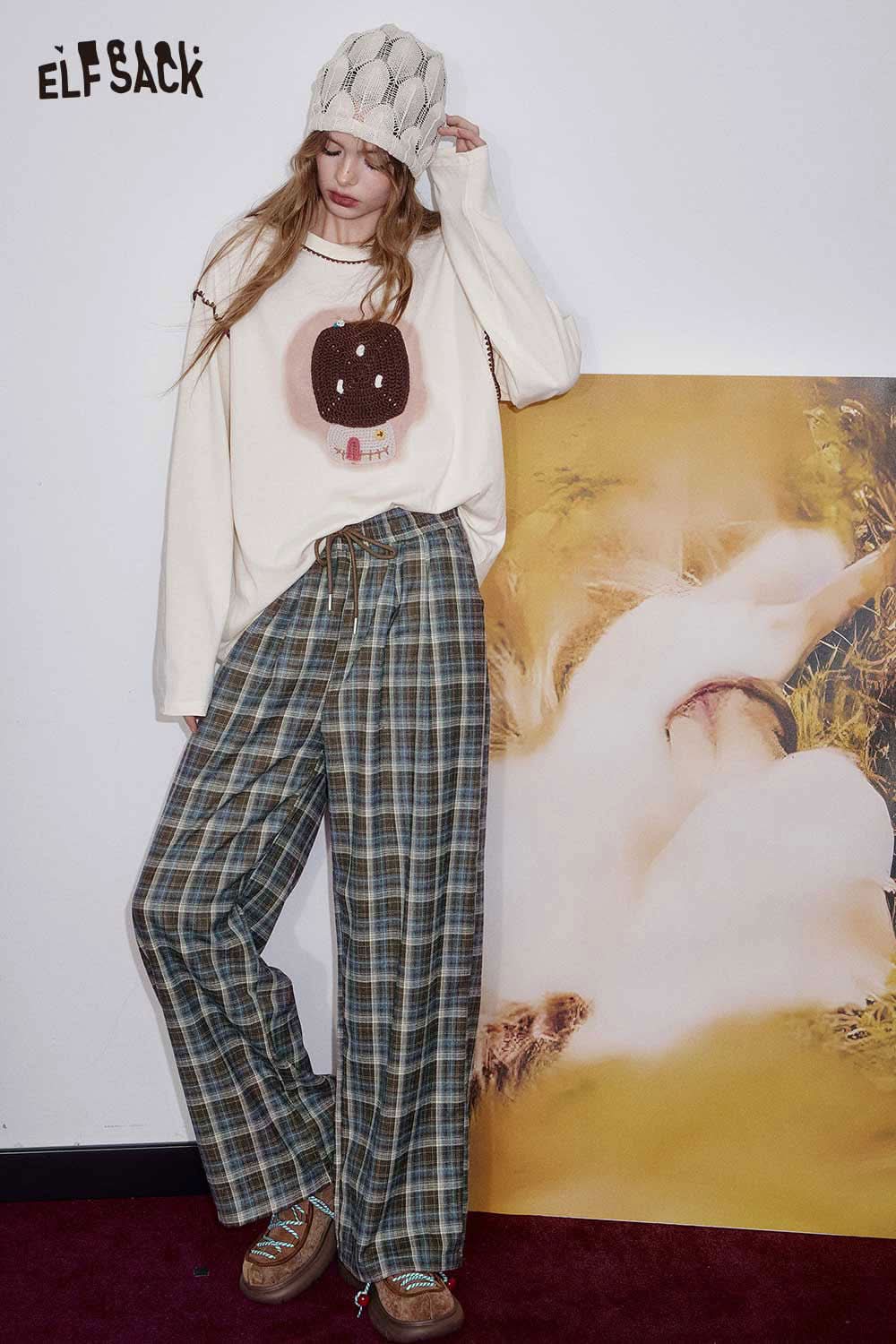 ELFSACK women's check pattern relaxed fit trousers paired with a playful graphic sweater and beanie.