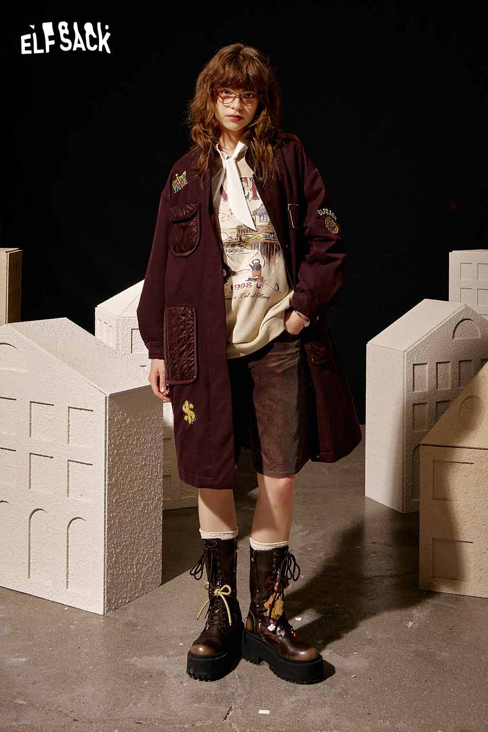 Model wearing a burgundy ELFSACK women's graphic sweatshirt with unique designs and stylish layers