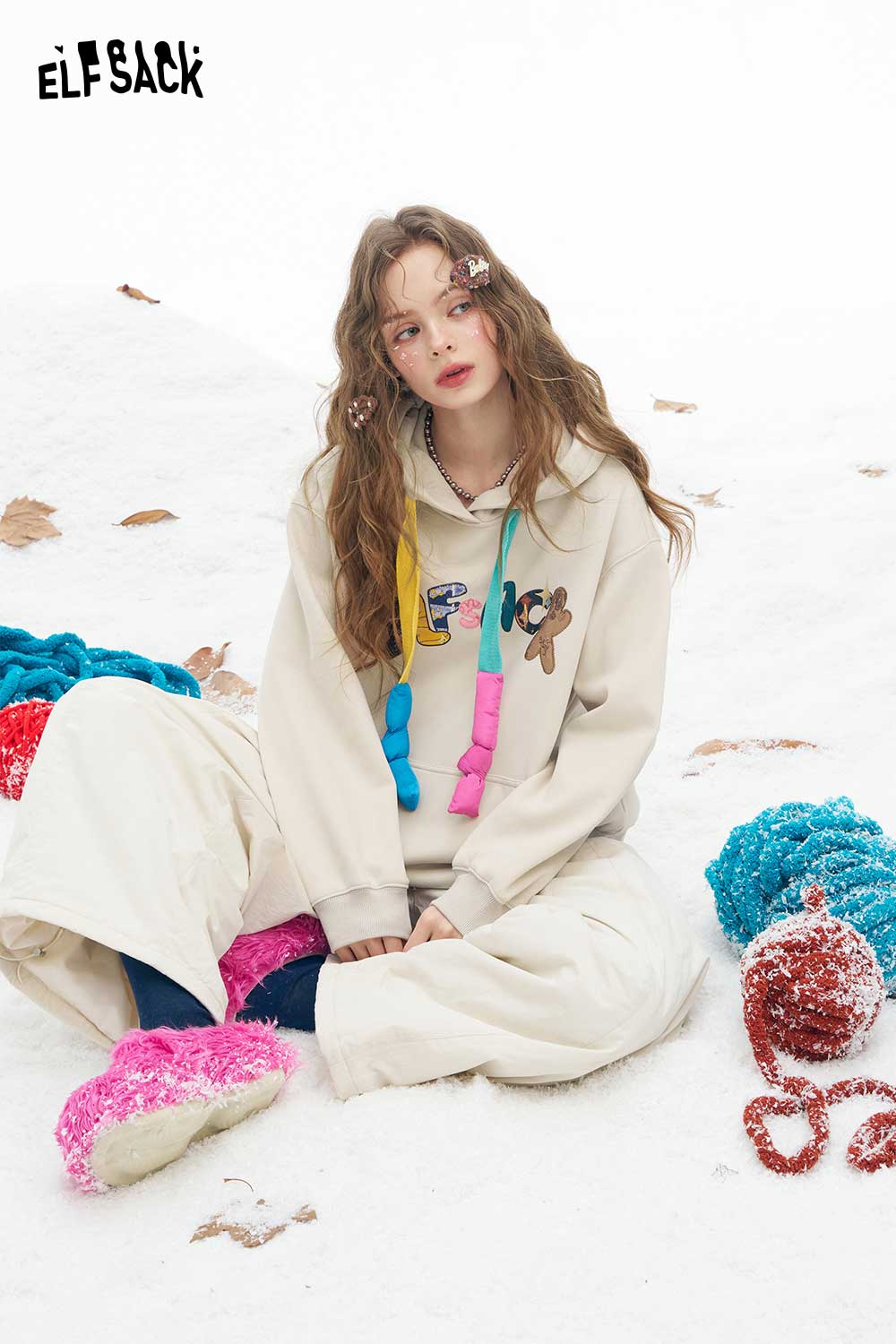 ELFSACK women's letter graphic hoodie in beige, styled with colorful accessories on snow-covered ground
