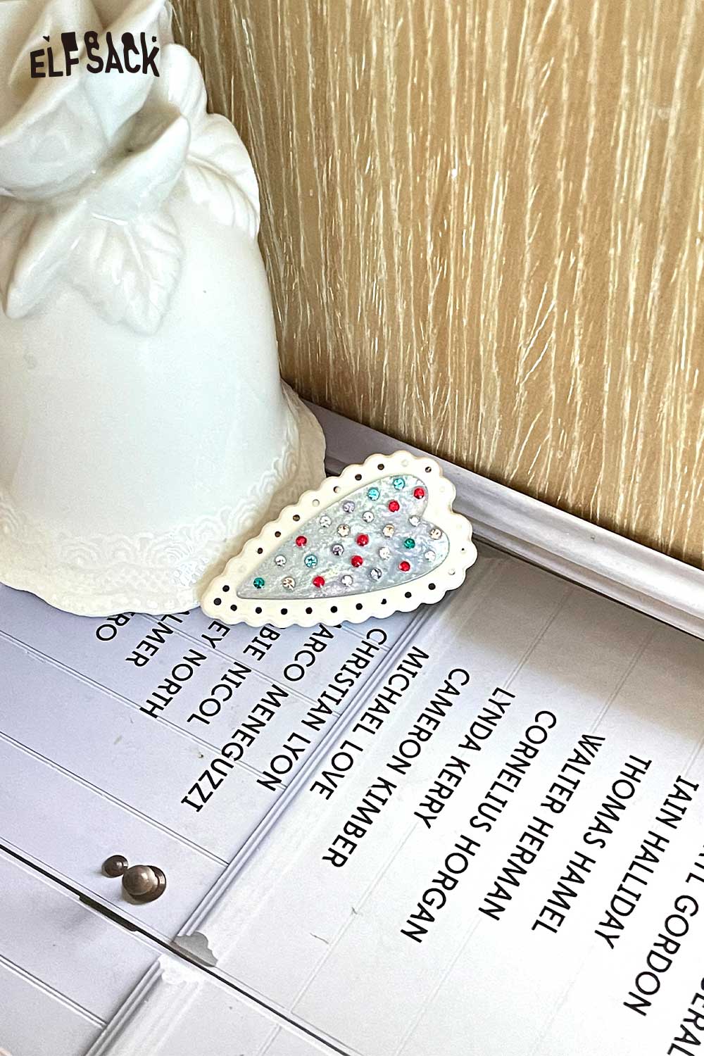 ELFSACK white scalloped heart hairpin with multicolor crystals on book near ceramic vase crystal embellished heart hairpin