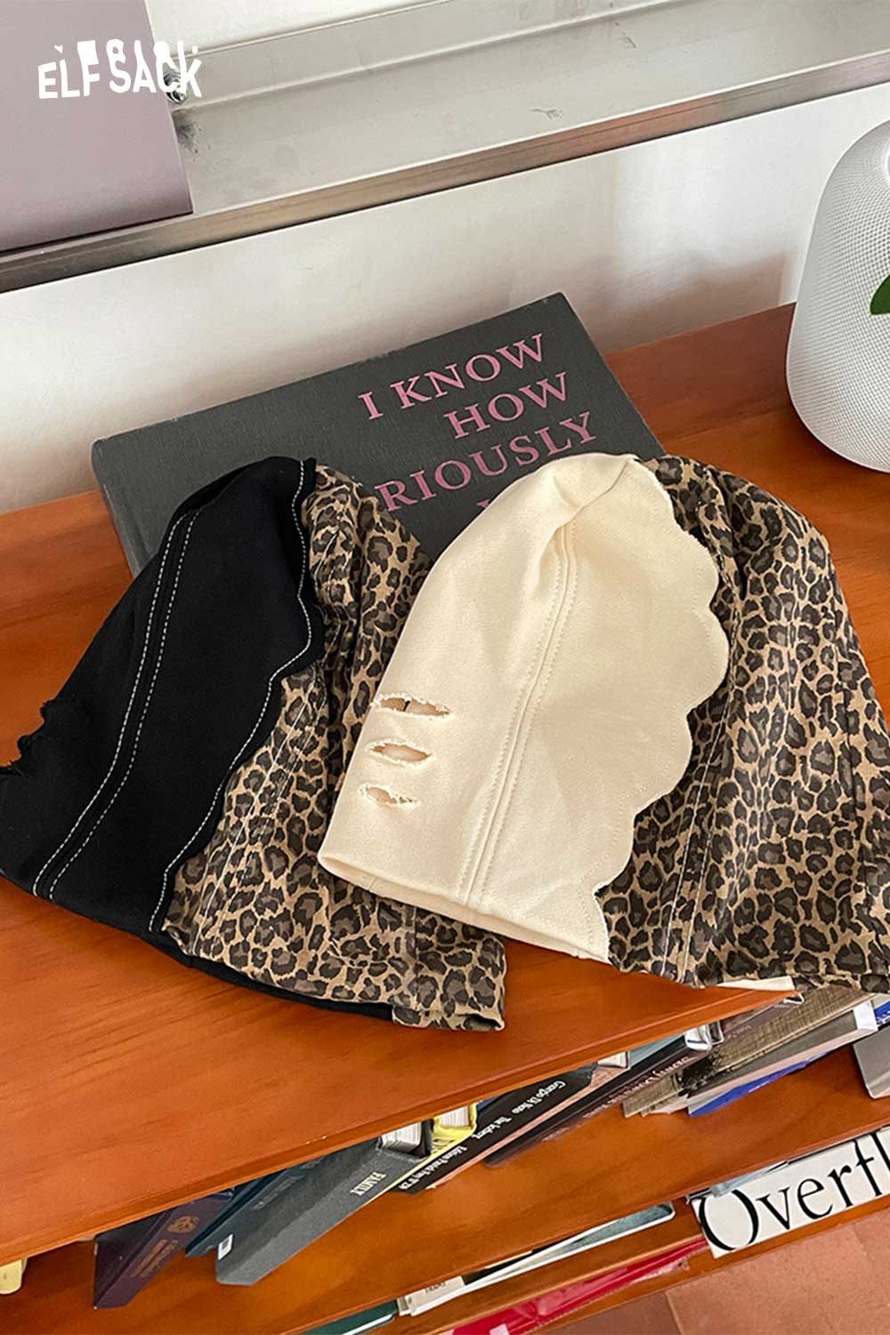 Three ELFSACK animal print slouchy beanie styles in black and beige on a wooden table