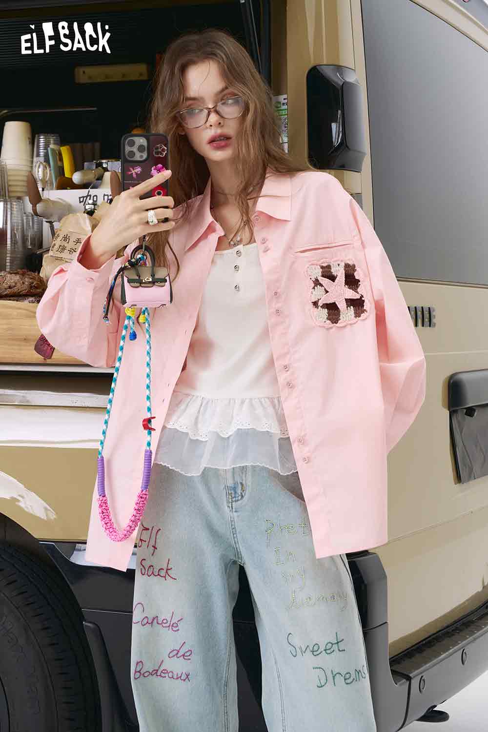 ELFSACK pink oversized 3D handmade crocheted shirt with chest crochet pocket layered over white ruffled top and jeans