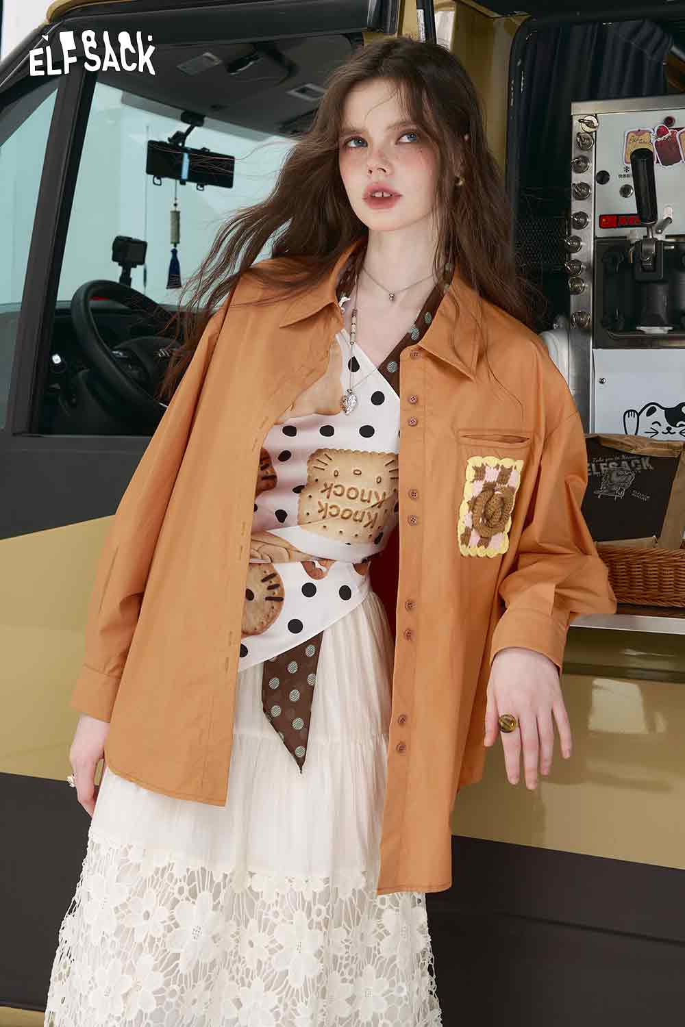 ELFSACK model wearing tan oversized shirt with lace skirt and polka dot top featuring 3D handmade crocheted shirt pocket detail