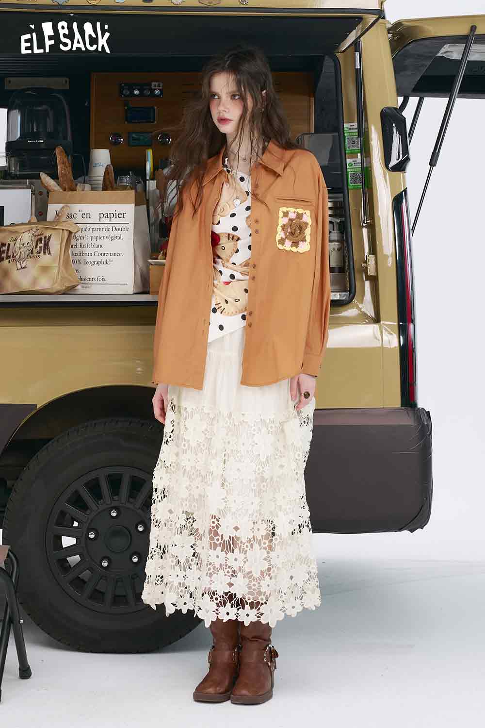 Model wearing a 3D handmade crocheted shirt in brown with floral pocket, layered over polka dot blouse and lace skirt
