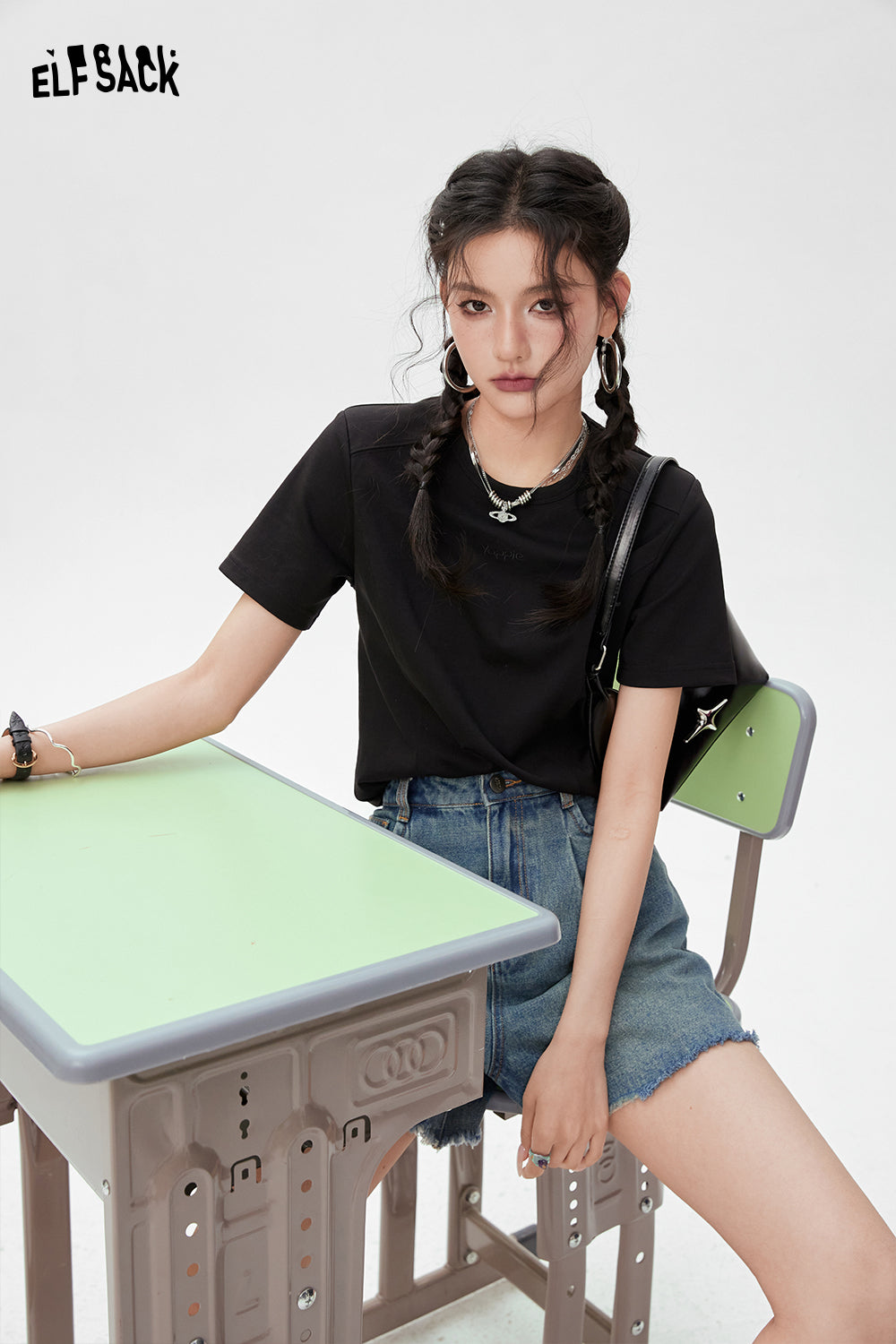 ELFSACK black BM Style T-shirt worn by woman sitting on green and gray school desk chair