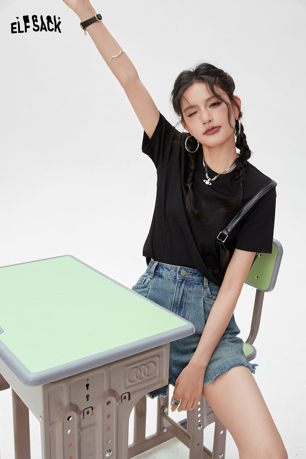 ELFSACK black BM Style T-shirt worn by woman with braided hair sitting on green chair